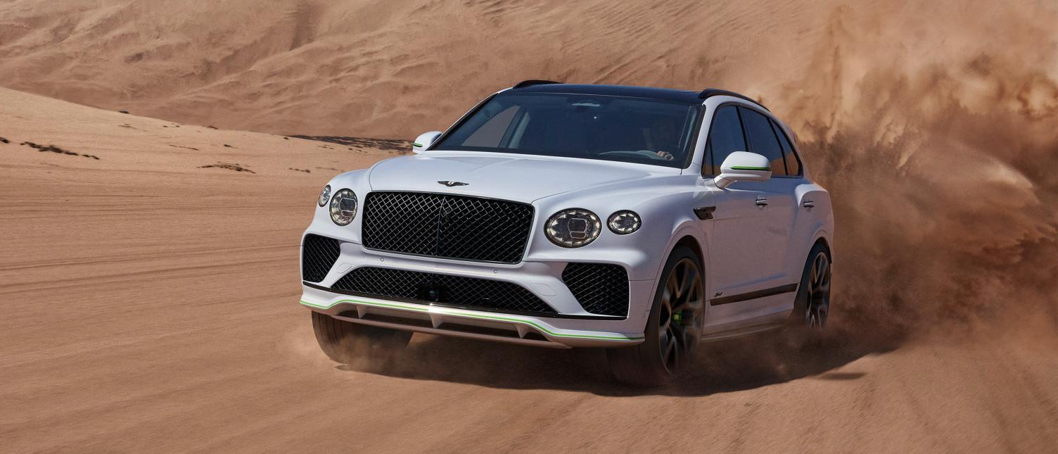 A white Bentley Bentayga driving across desert dunes, throwing up sand