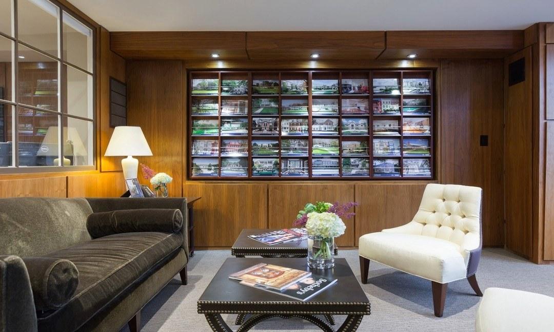 A Sotheby's International Realty office interior with an illuminated wall display of property listings above a seating area